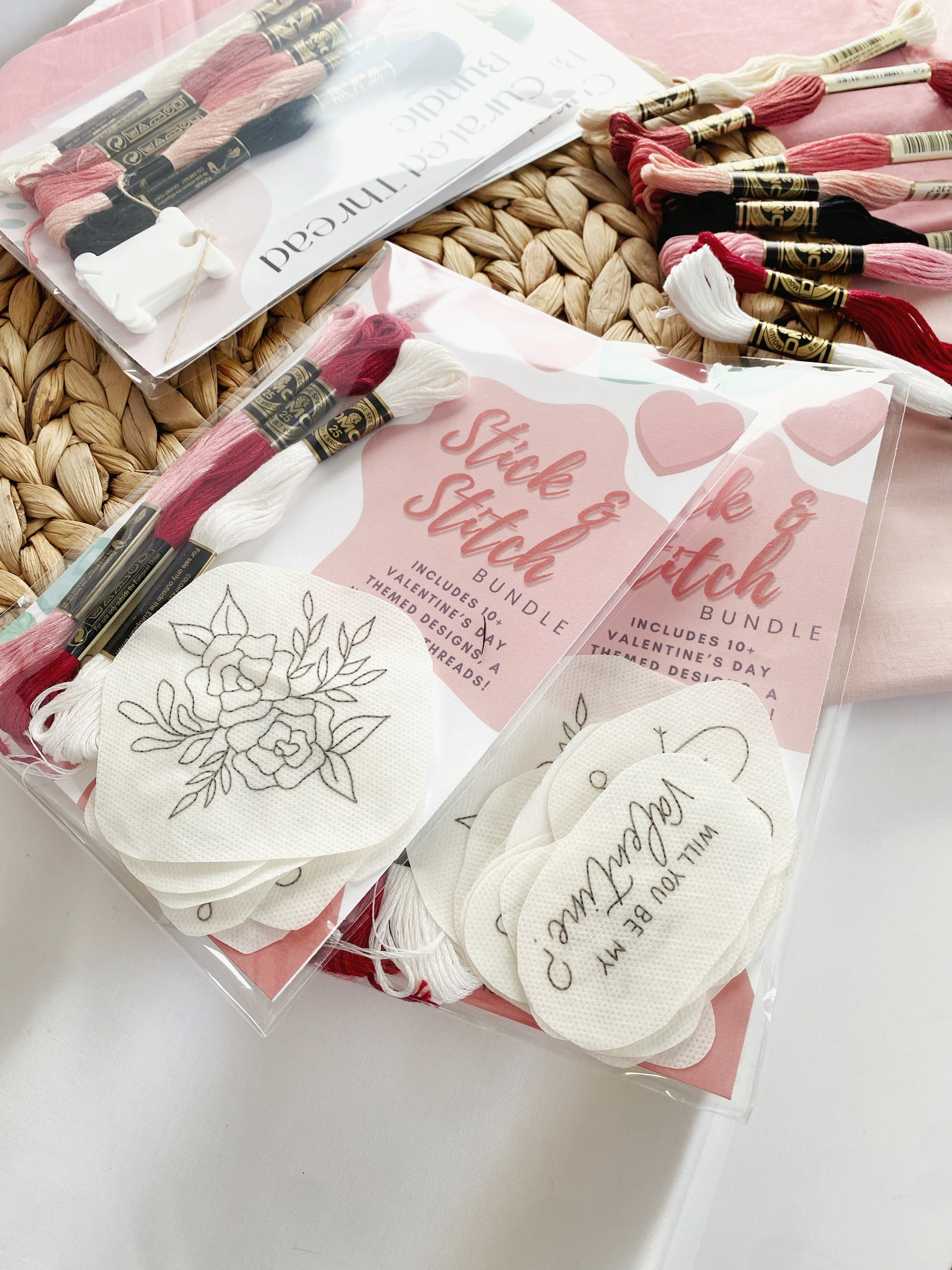 Homebody Handmade's Valentine's Stick and Stitch Pack is pictured on woven trivet. A variety of DMC threads in complimentary colours are shown and there are a number of different designs featured in the package.