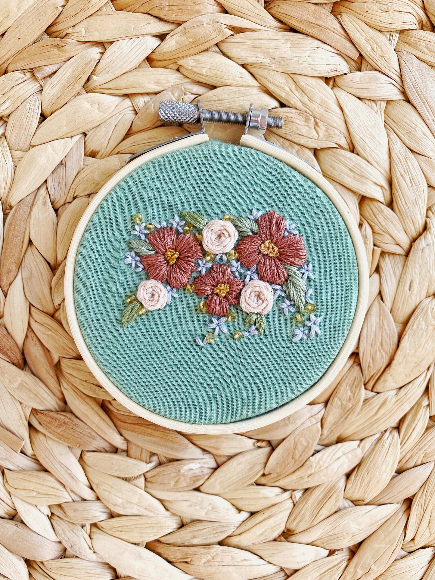 A bear is embroidered out of flower shapes and framed on green fabric in an embroidery hoop on a textured background. 