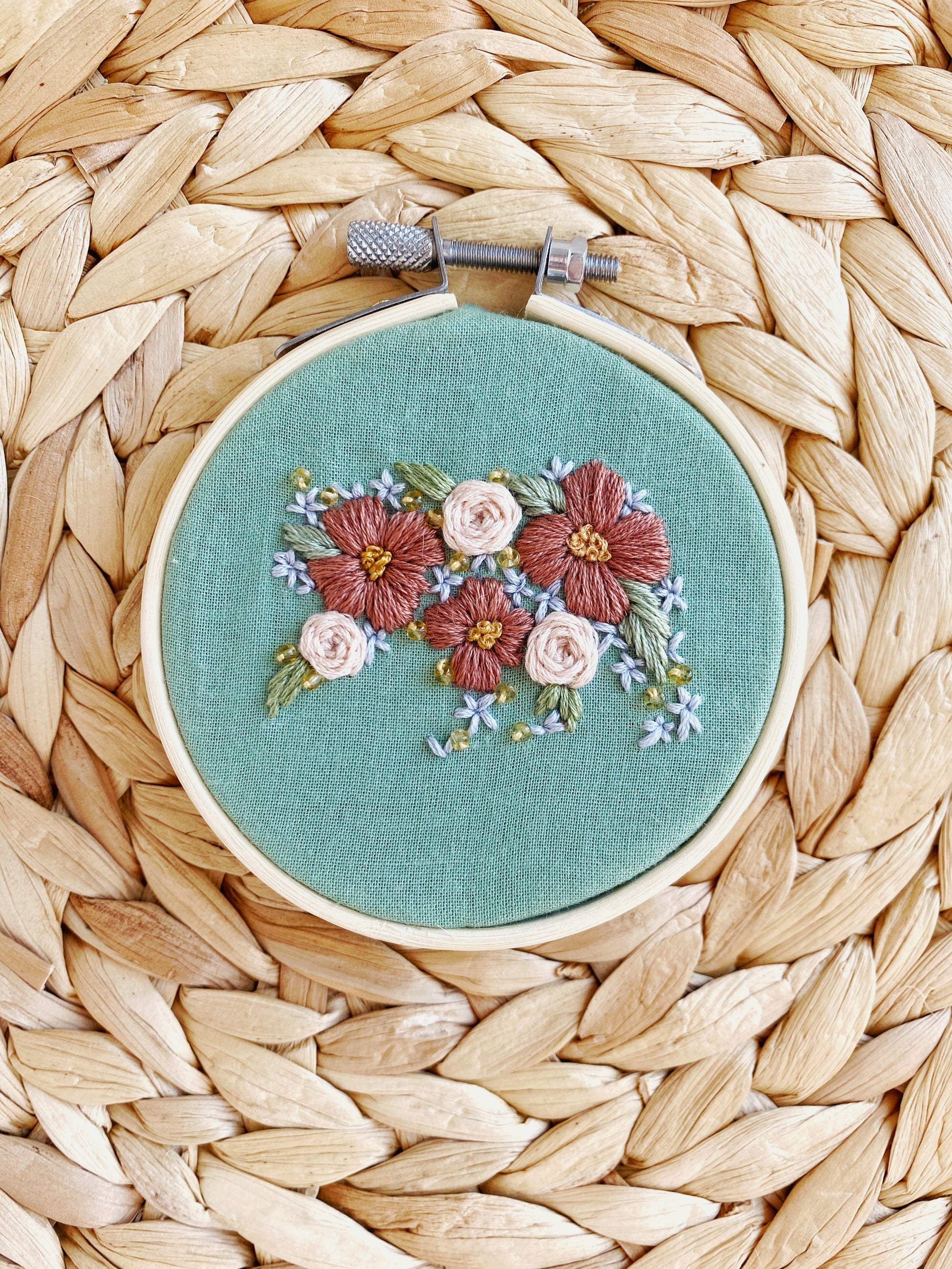 A bear is embroidered out of flower shapes and framed on green fabric in an embroidery hoop on a textured background. 