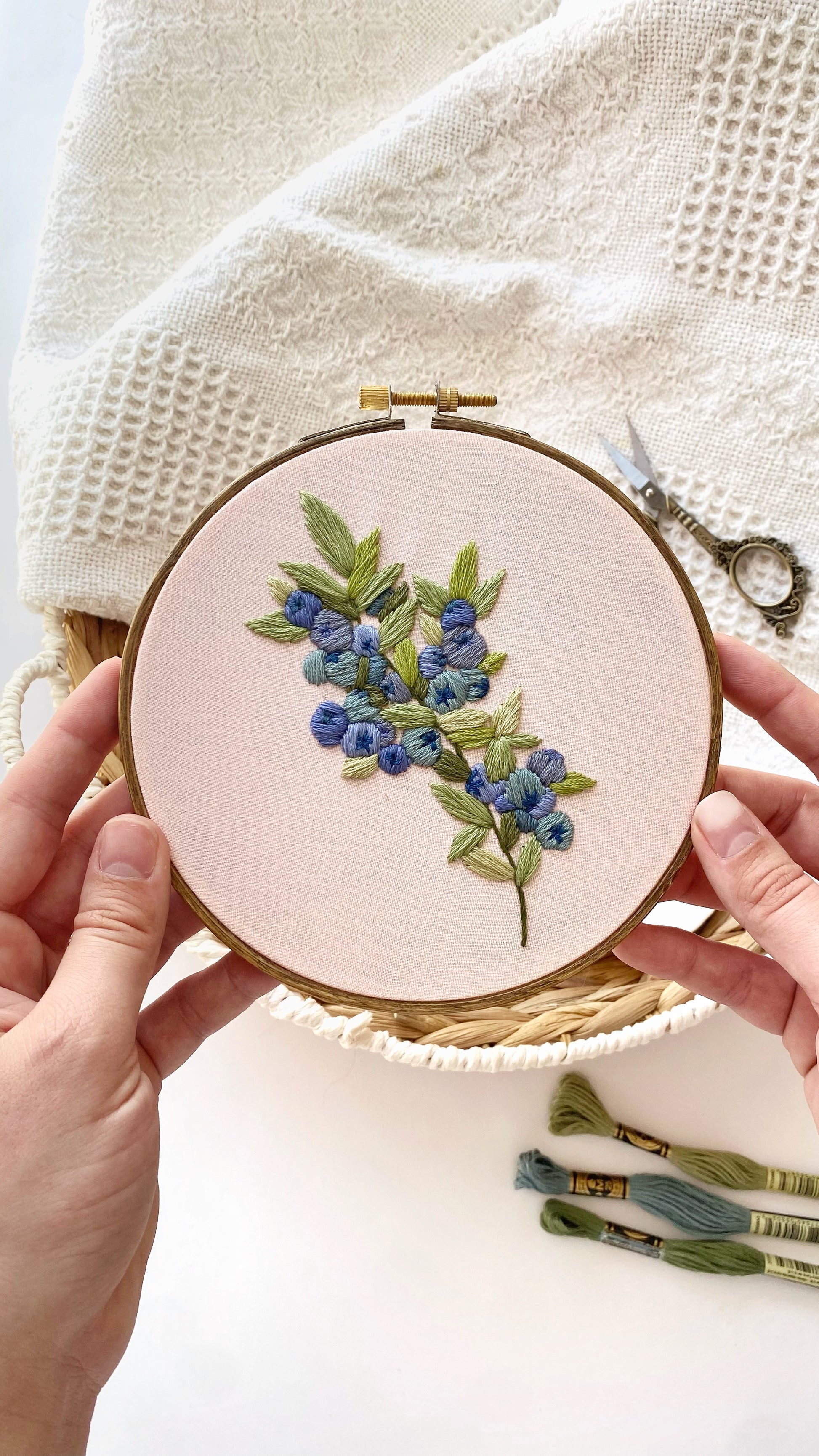 Embroidery hoop with blueberry design held by hands on a light background