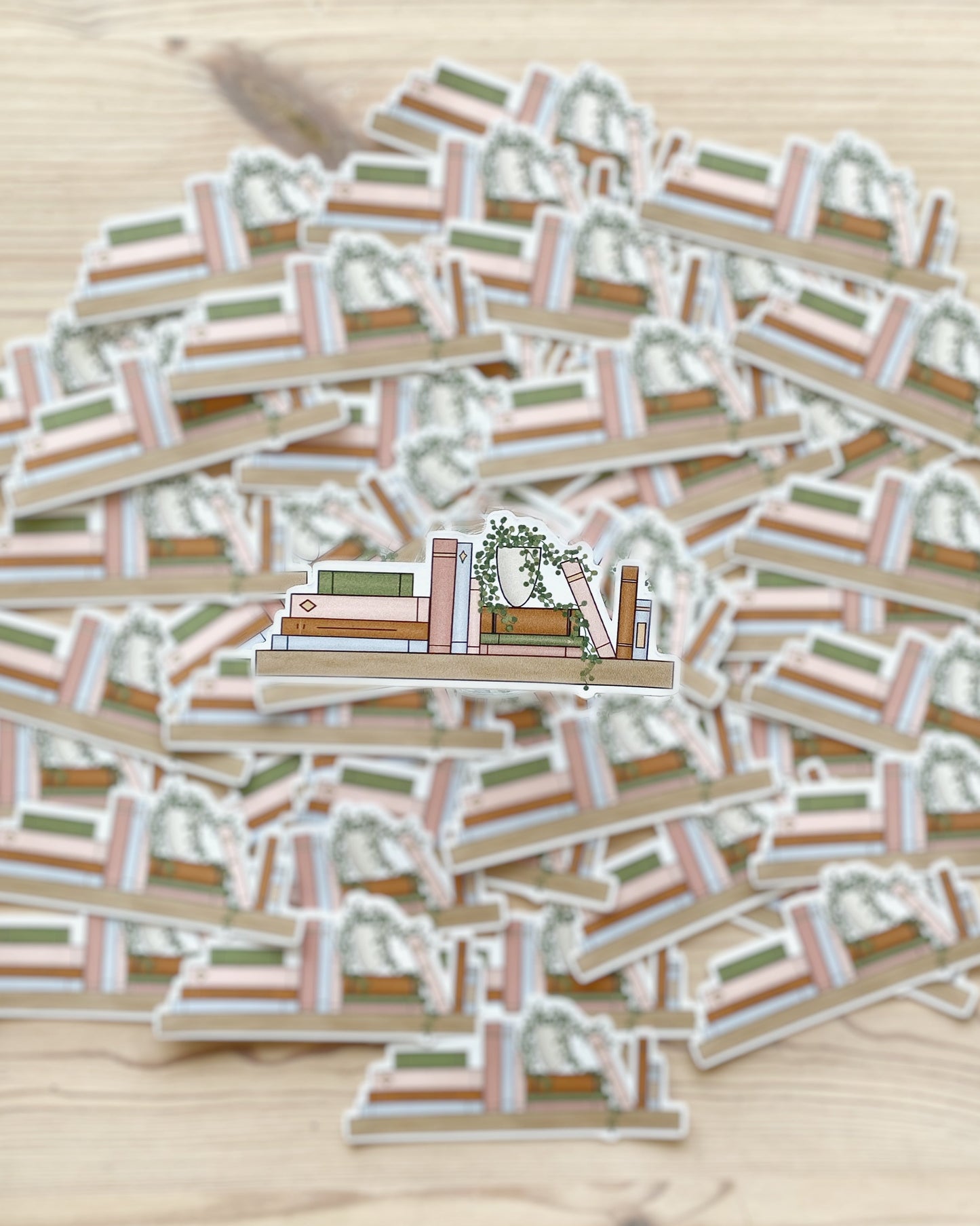 An illustrated bookshelf sticker featuring a variety of books and a potted plant is clearly in the foreground of the image with matching stickers spread out and blurred in the background.