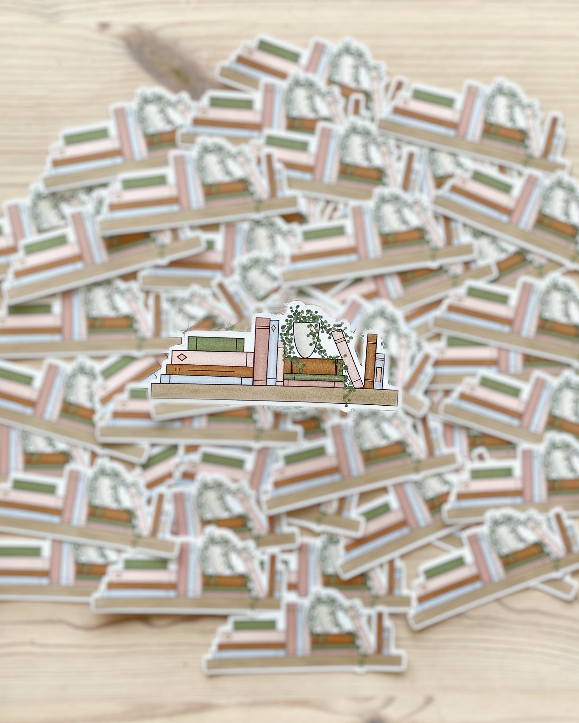 An illustrated bookshelf sticker featuring a variety of books and a potted plant is clearly in the foreground of the image with matching stickers spread out and blurred in the background.