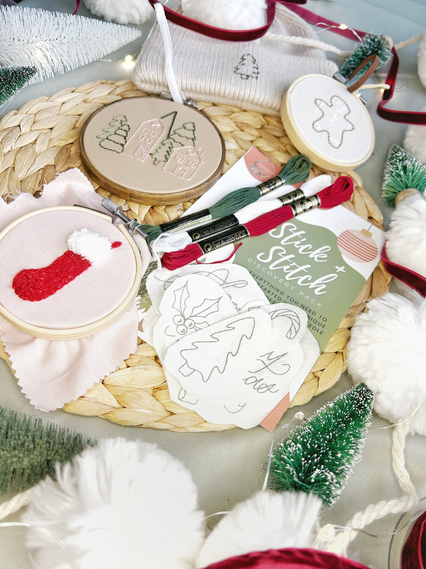 A Christmas themed Stick and Stitch embroidery kit is shown on a textured surface with a variety of finished embroidered projects and surrounded by seasonal decor.