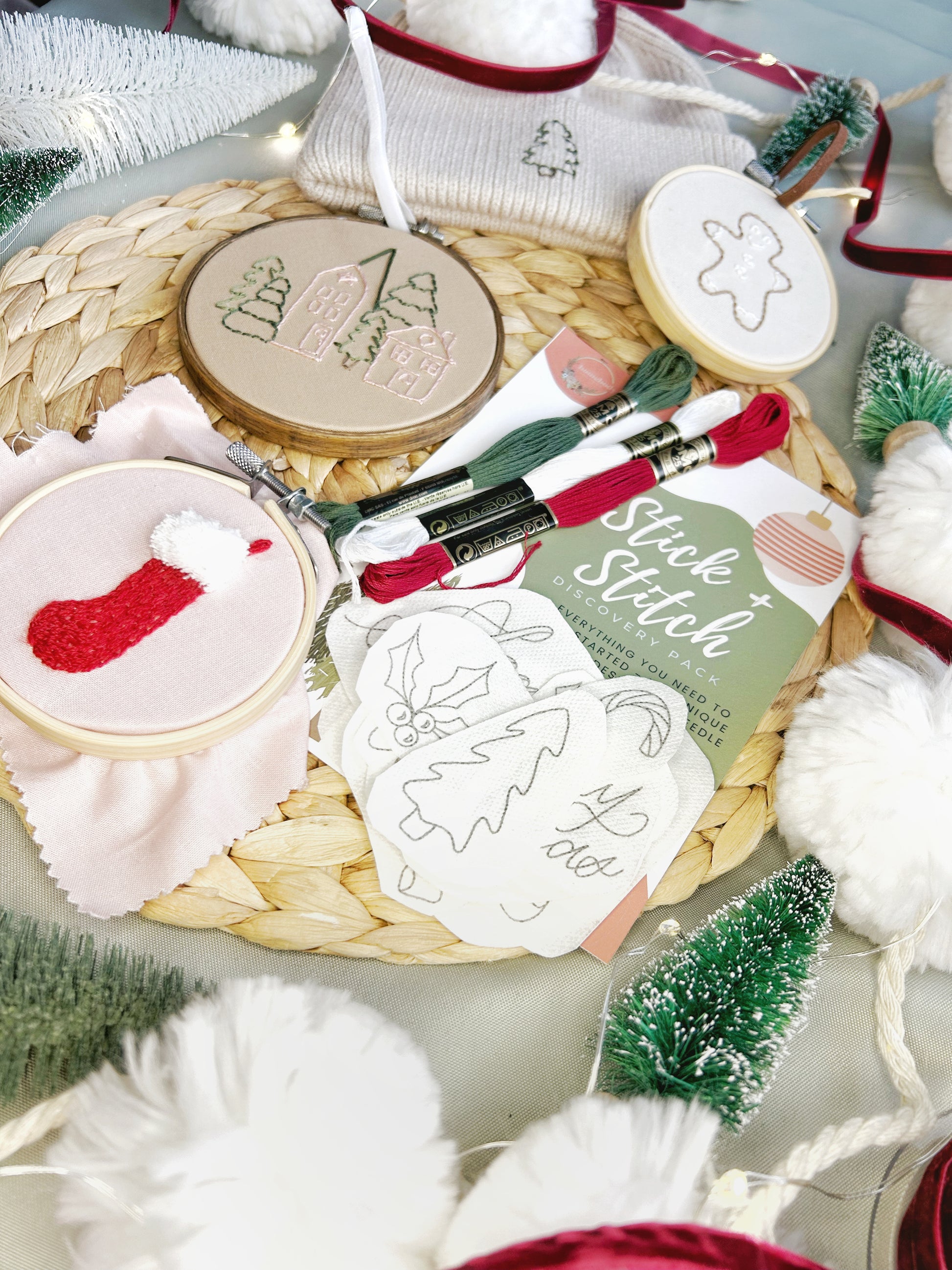 A Christmas themed Stick and Stitch embroidery kit is shown on a textured surface with a variety of finished embroidered projects and surrounded by seasonal decor.