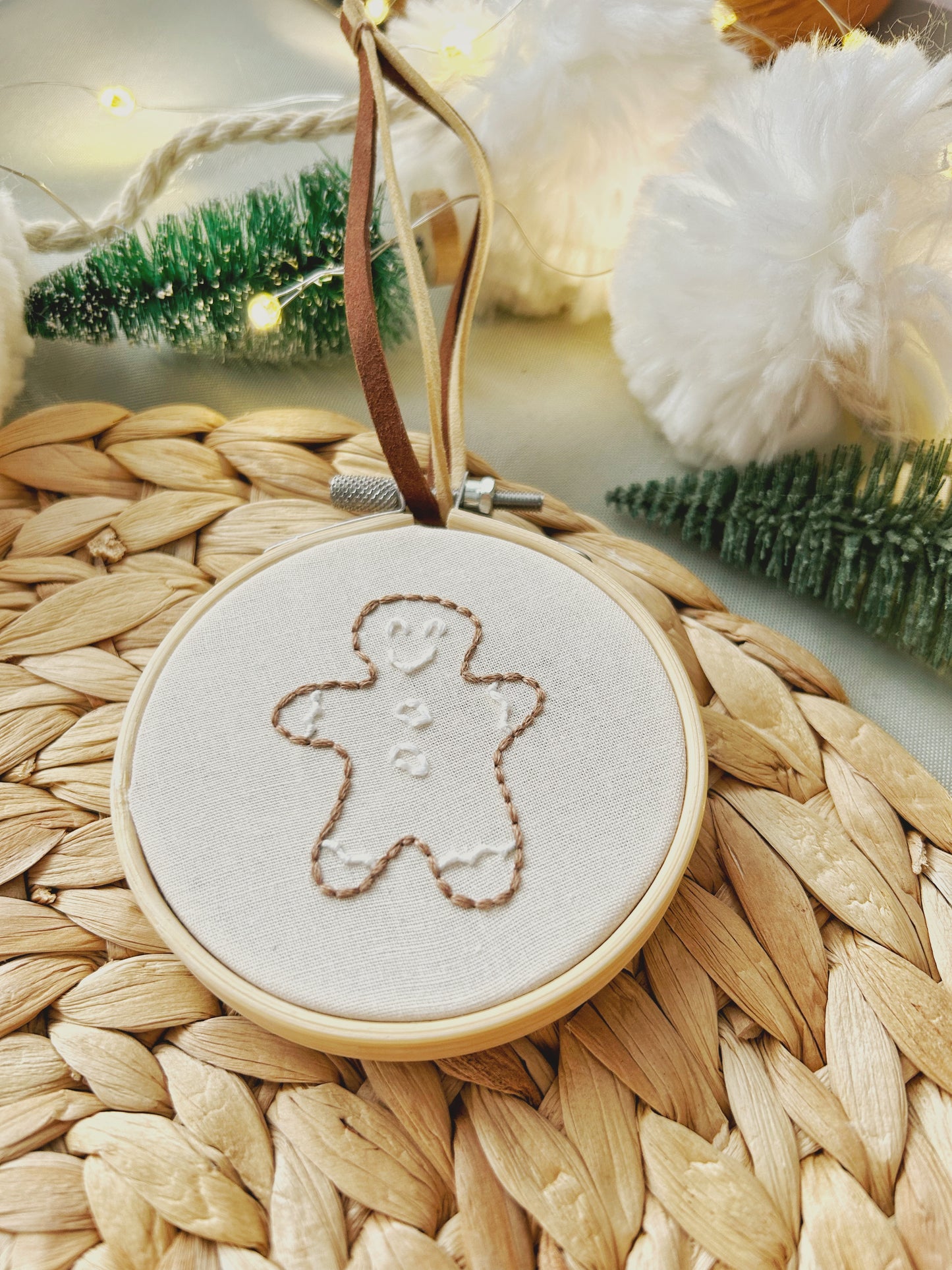 A close up of an embroidered gingerbread cookie made with a stick and stitch kit is on a textured surface and surrounded by seasonal decorations.