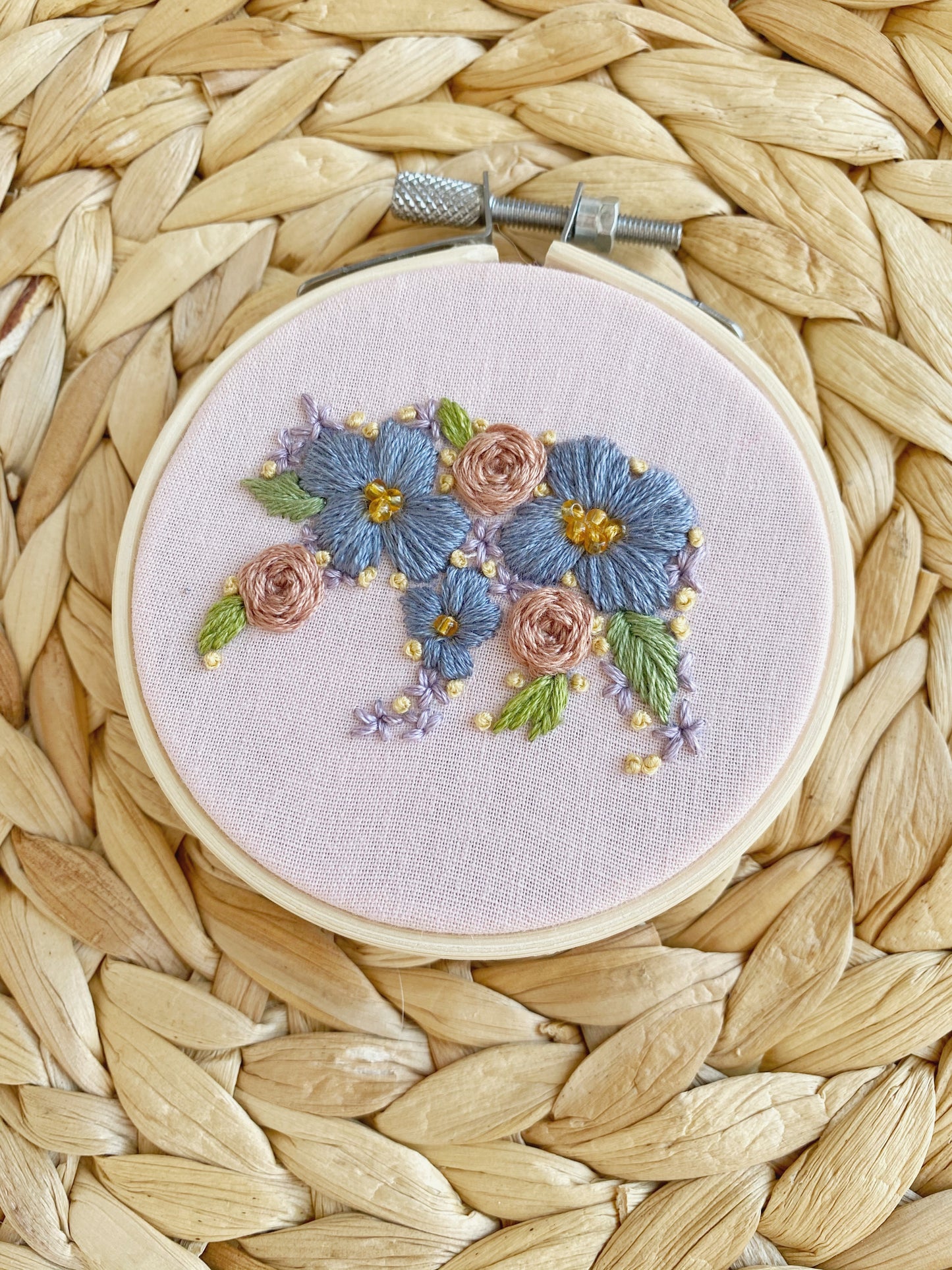 The silhouette of a bear is embroidered out of floral shapes and framed on light pink fabric in an embroidery hoop and displayed on a woven textured backgrount.