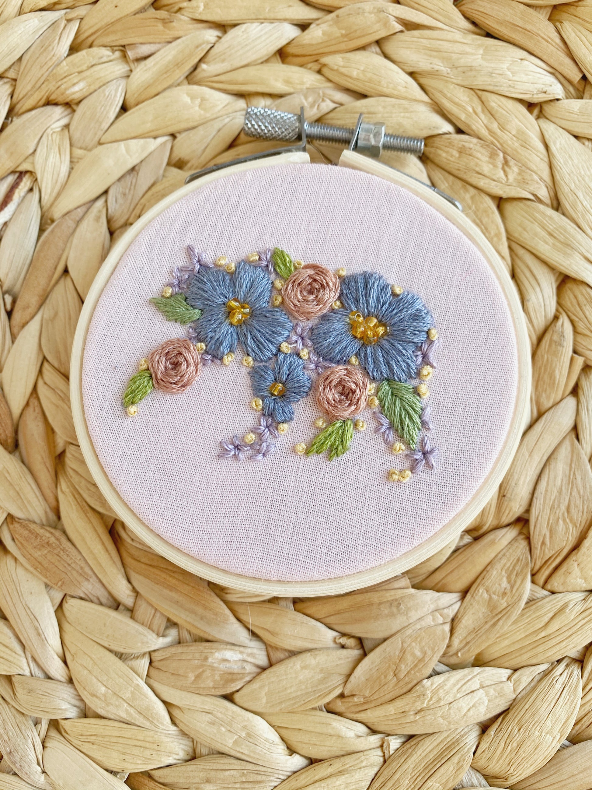 The silhouette of a bear is embroidered out of floral shapes and framed on light pink fabric in an embroidery hoop and displayed on a woven textured backgrount.