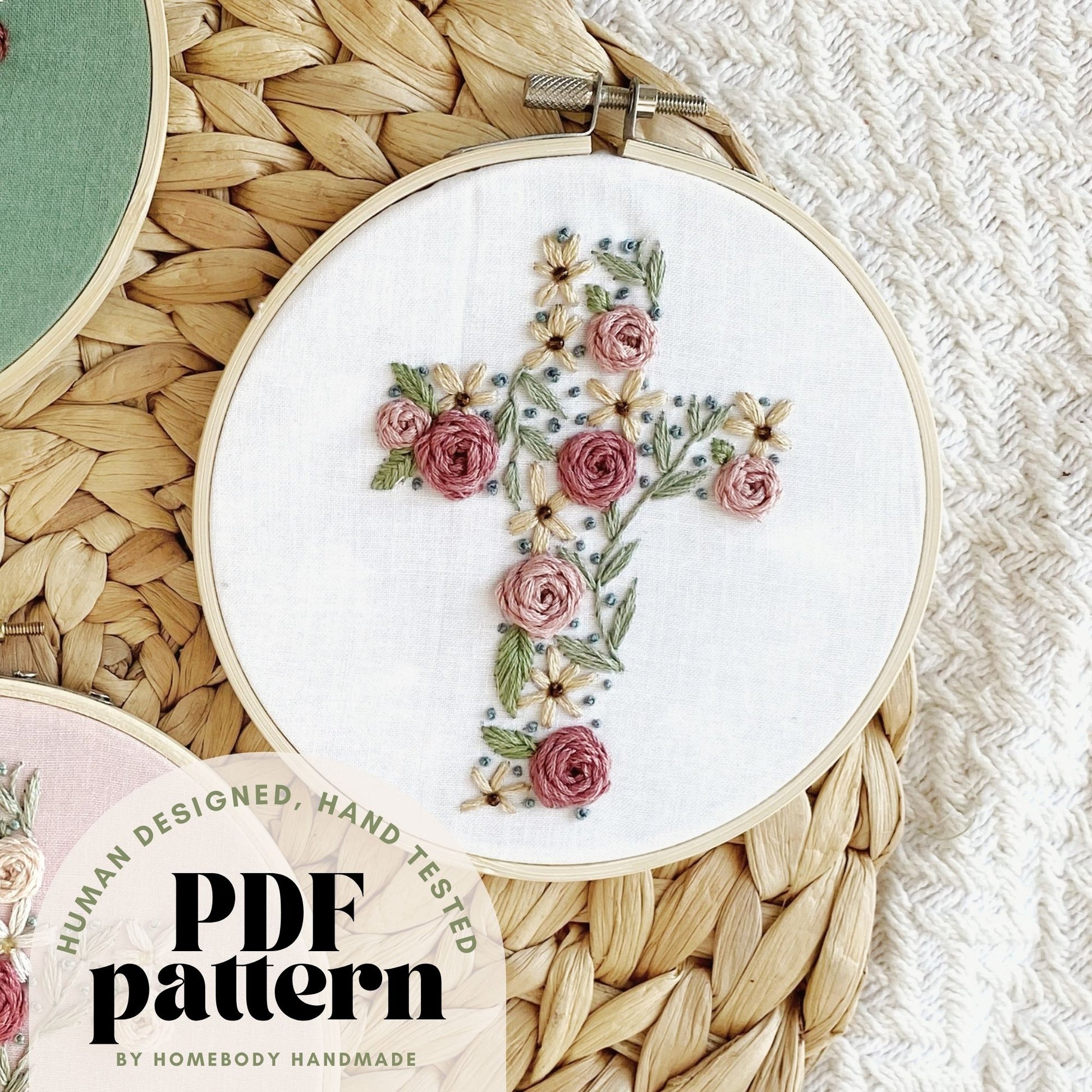 Embroidery hoop with floral cross design on a textured surface, text overlay denotes "hand tested, human designed PDF pattern by Homebody Handmade."