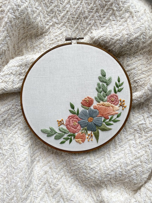 An embroidery hoop featuring a floral arrangement in a crescent swooping up the bottom right edge of the hoop.