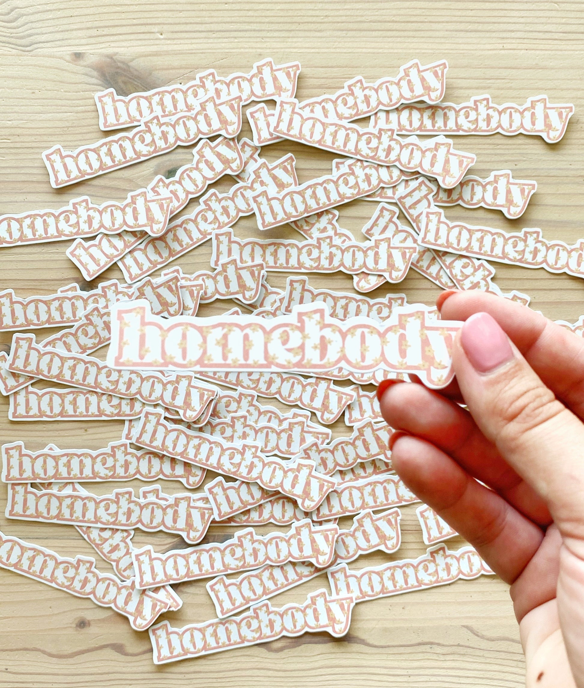 Hand holding a vinyl homebody sticker with little flowers on it.