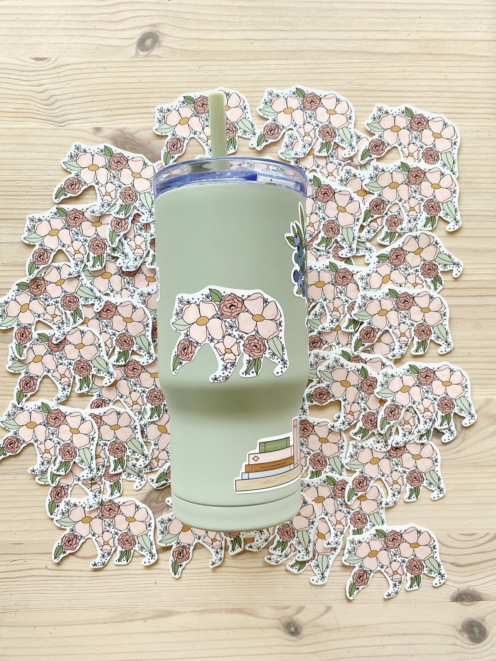 Sage green tumbler featuring a floral mama bear sticker, shown with additional matching stickers in the background.
