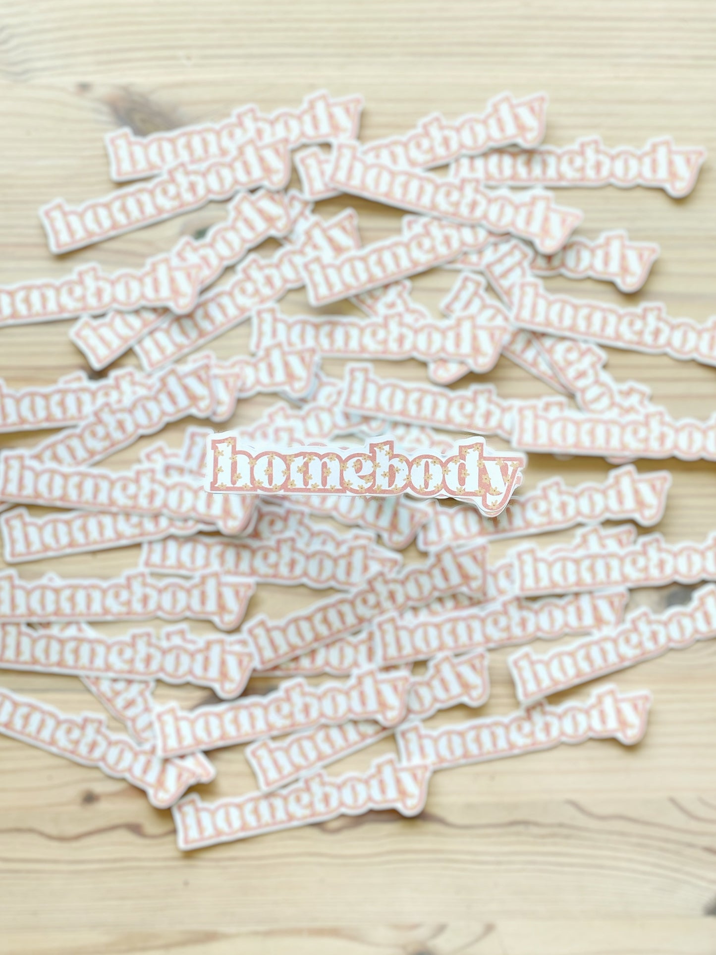 A sticker with the word "homebody" is in the foreground of this image with multiple matching stickers blurred in the background. 