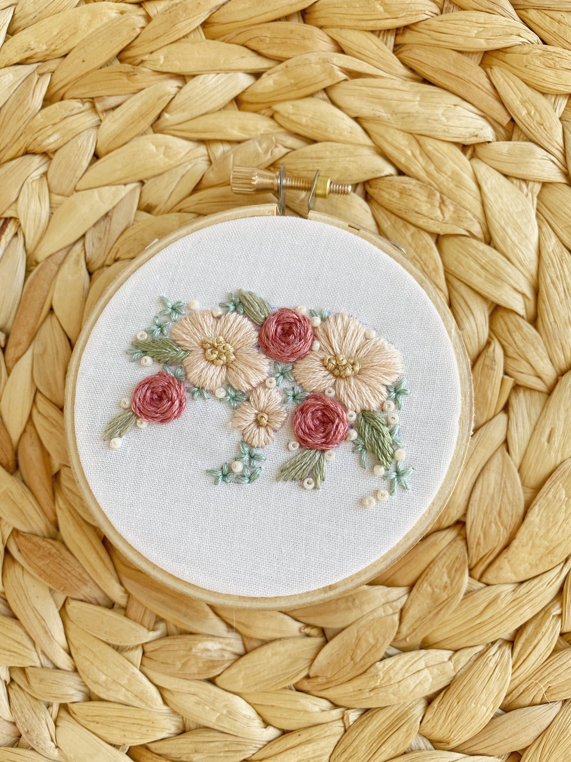 A bear silhouette is filled in with embroidered flowers and framed in an embroidery hoop displayed on a textured background.
