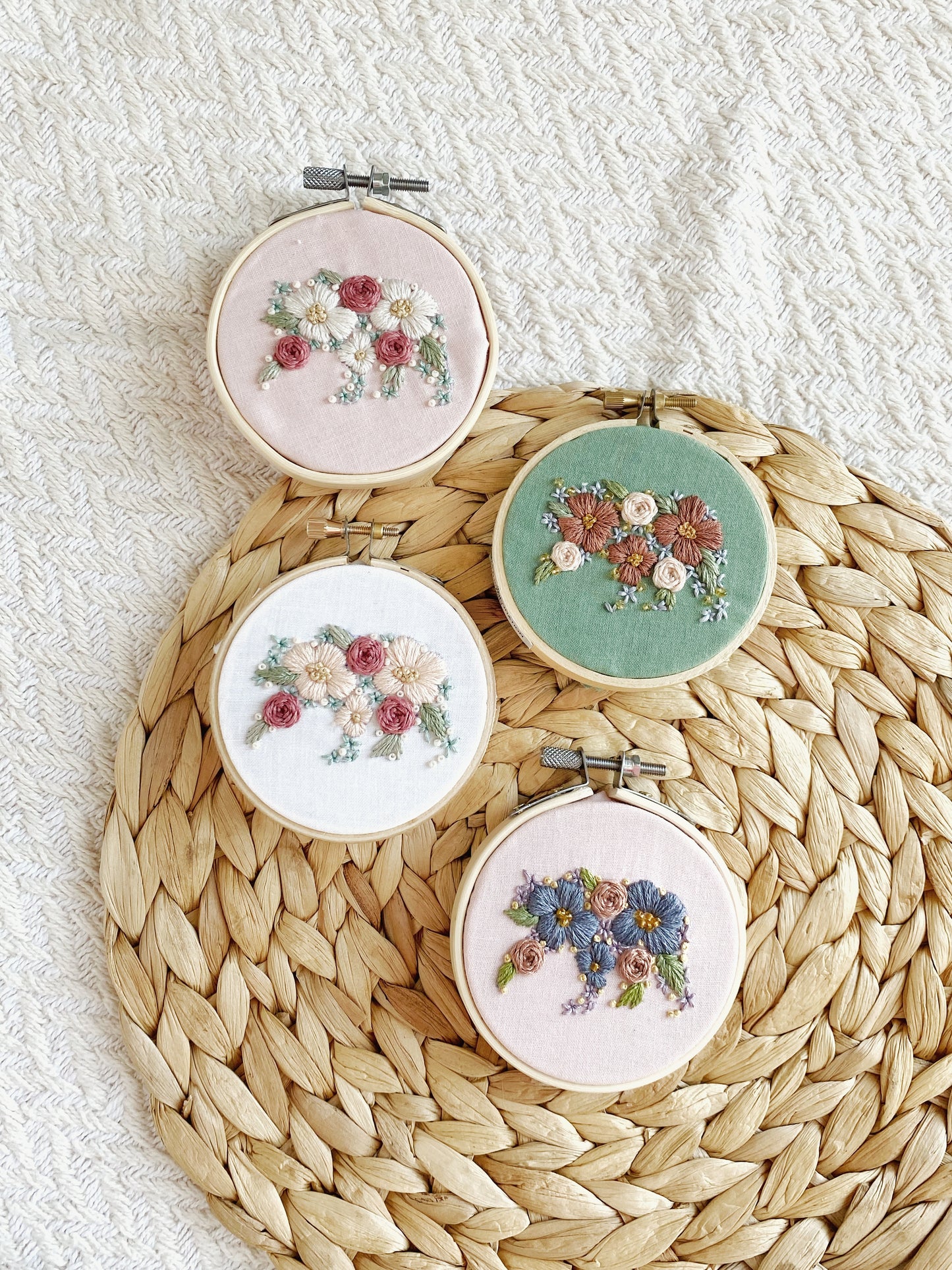 Four embroidered bear silhouettes in pink, white, and green, framed in beige hoops, displayed on a woven beige background.