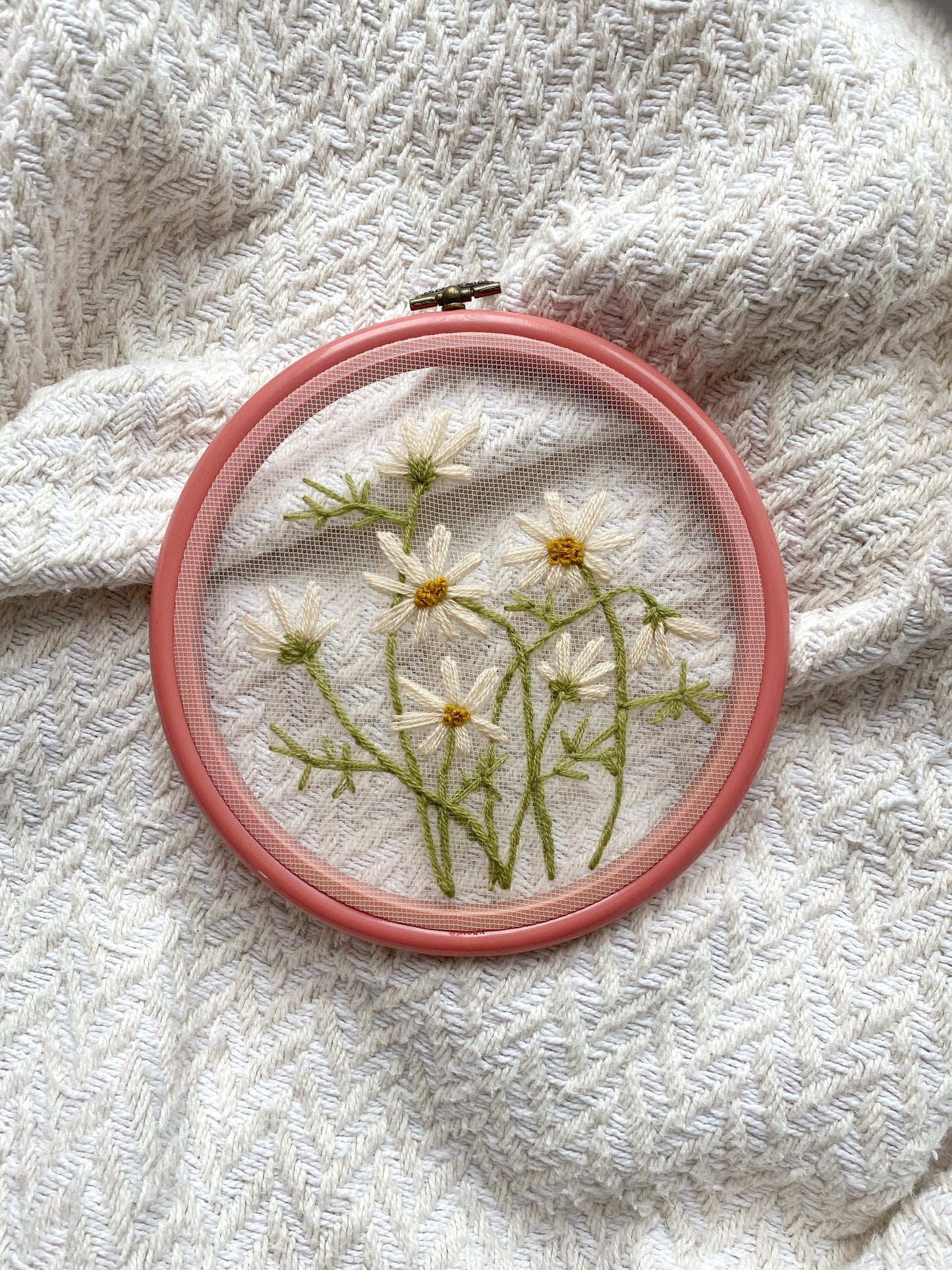 Embroidery hoop art with daisy flowers on a white tulle fabric, secured within a pink 6-inch vintage hoop.