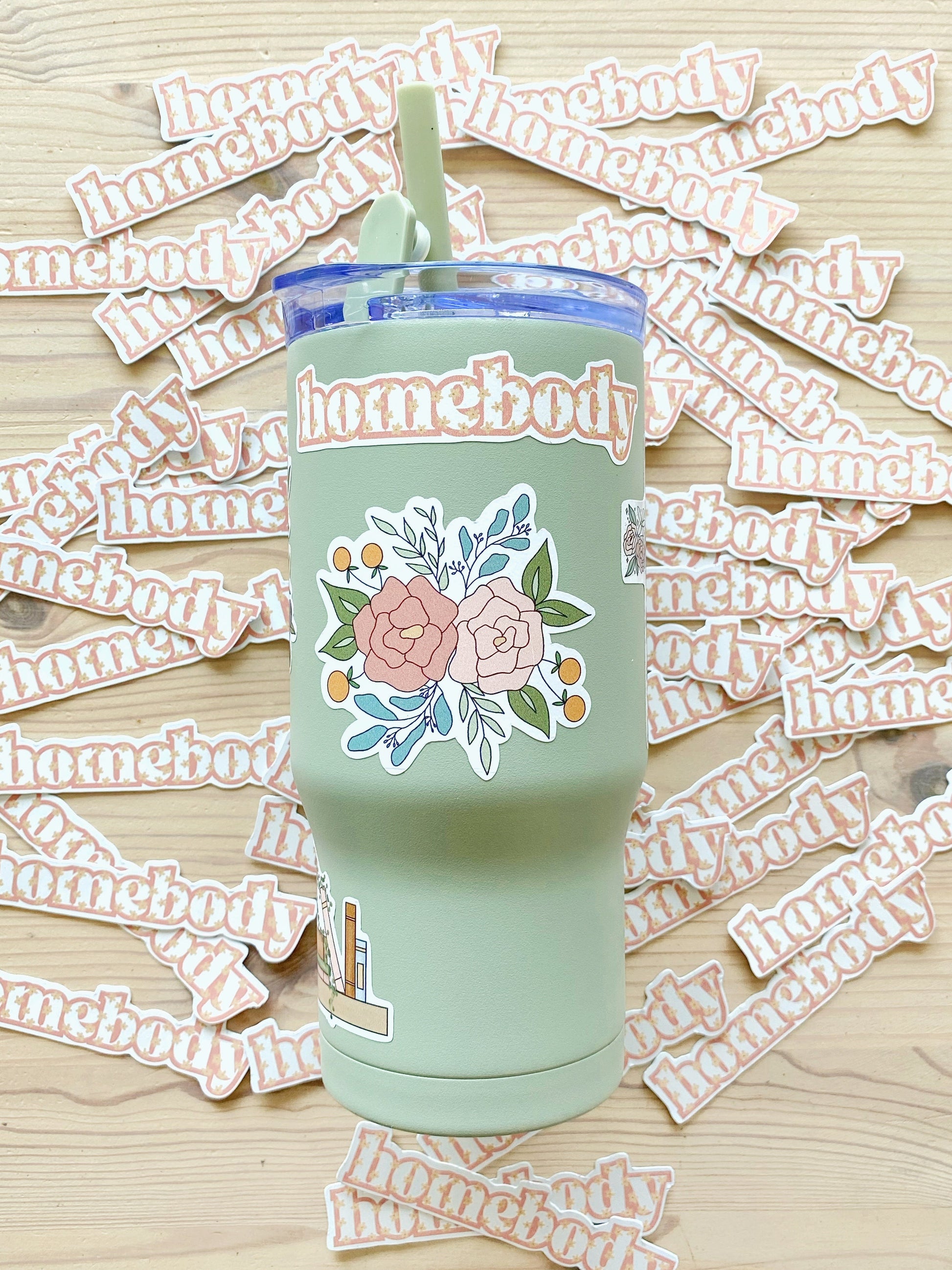 Light green tumbler with floral and ‘homebody’ stickers, matching homebody stickers are spread out in the background.