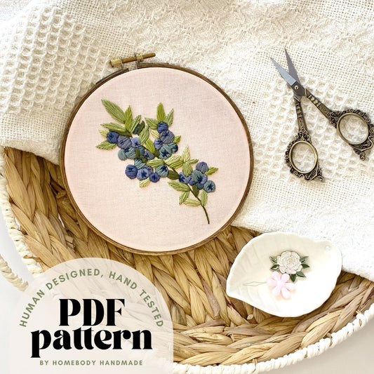 Embroidery hoop with blueberry design on a textured surface with scissors and fabric.