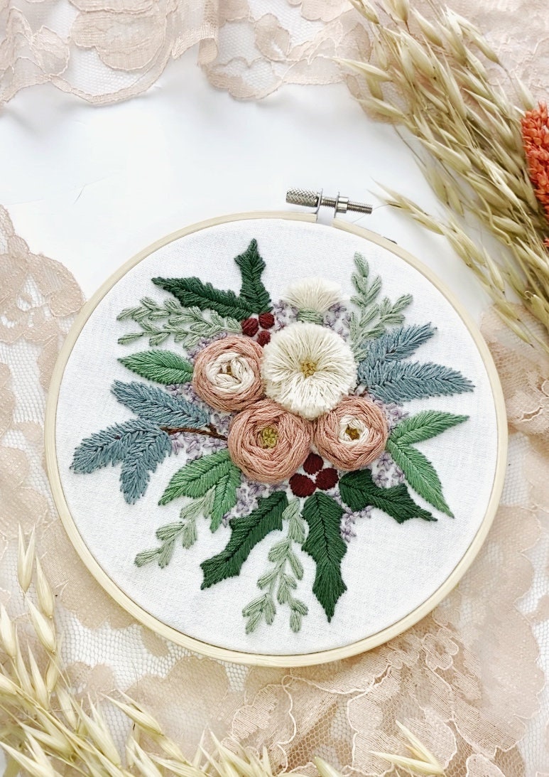 a variety of embroidered flowers and wintry greenery are stitched onto white fabric displaying the artist's work with texture and colour for embroidery inspo.