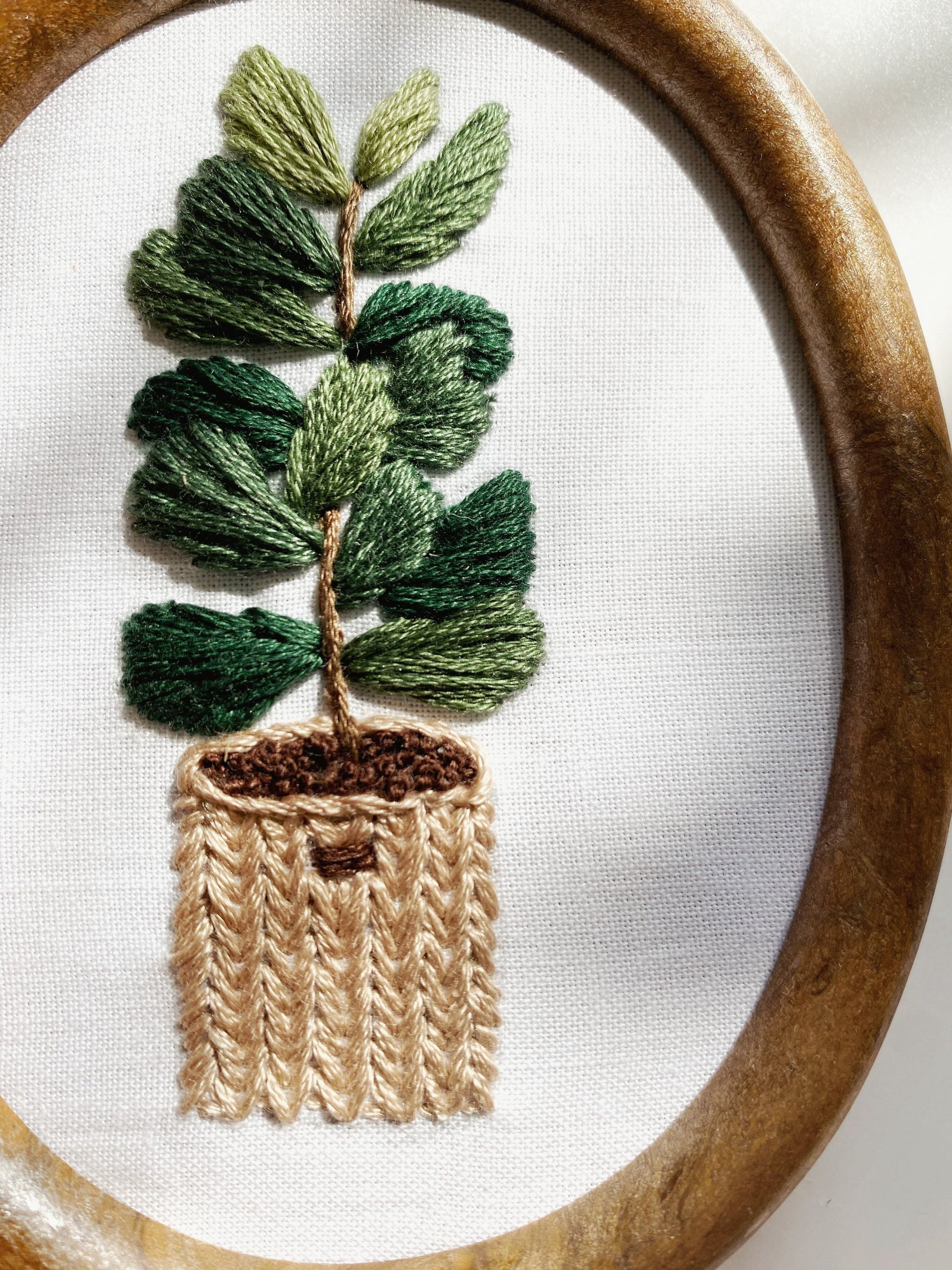 A close up of a  finished embroidery pattern featuring a fiddle leaf fig plant in a basket is dappled in sunlight for embroidery project inspiration. 