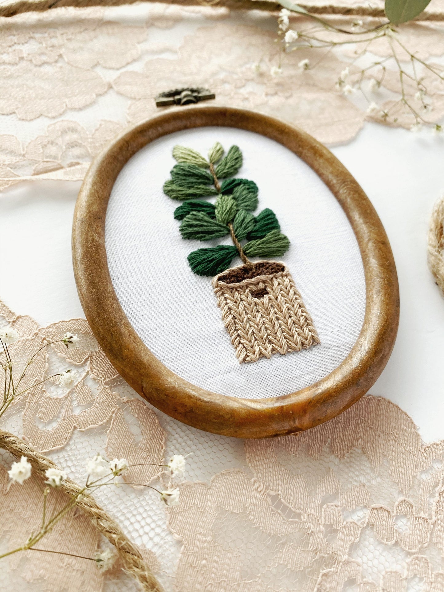 A finished embroidery hoop of a fiddle leaf fig potted in a basket displayed artfully for embroidery pattern inspiration.