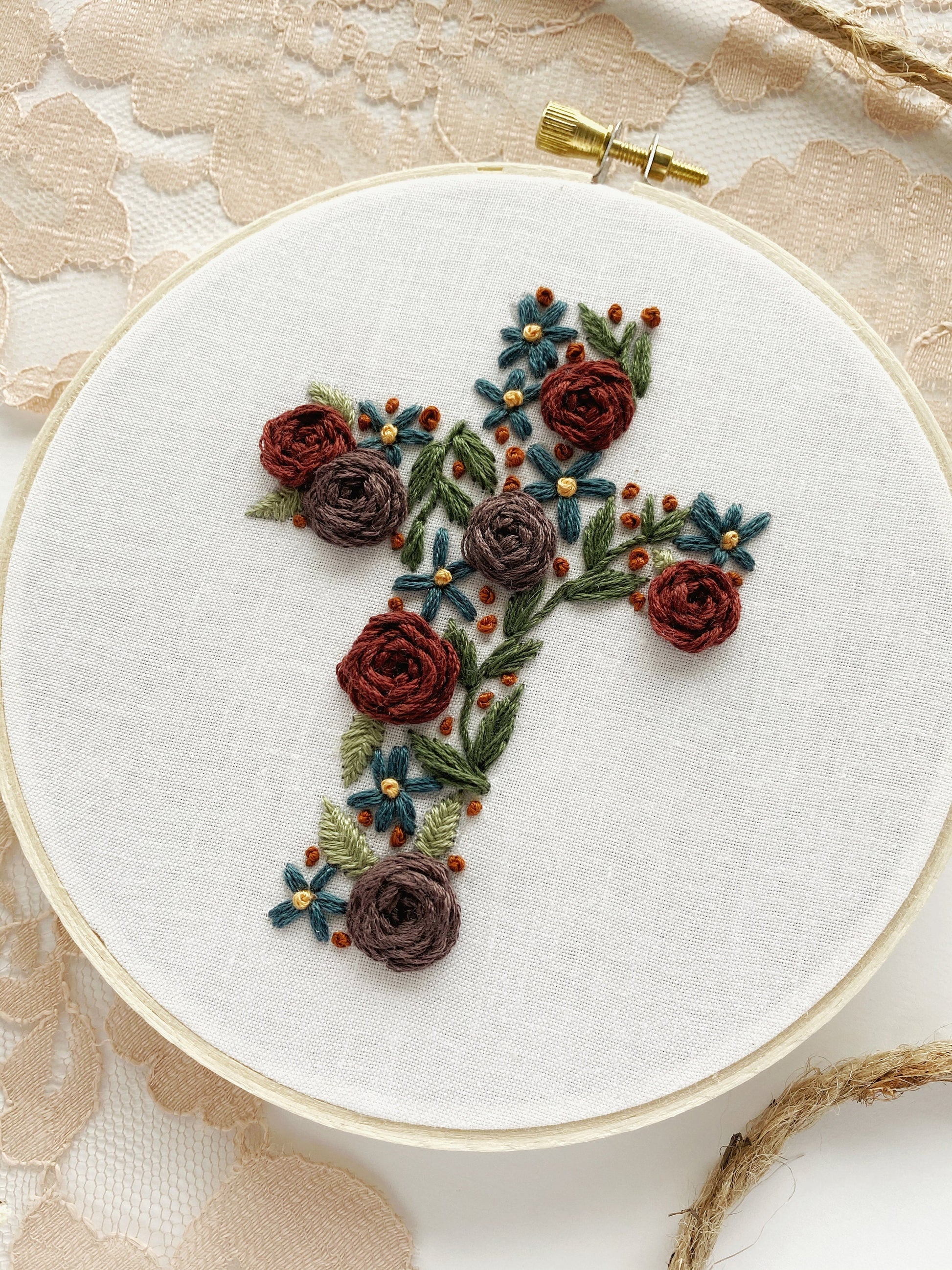 Close-up of a floral cross embroidery hoop in deep, muted rainbow colours, perfect for beginner stitching projects.