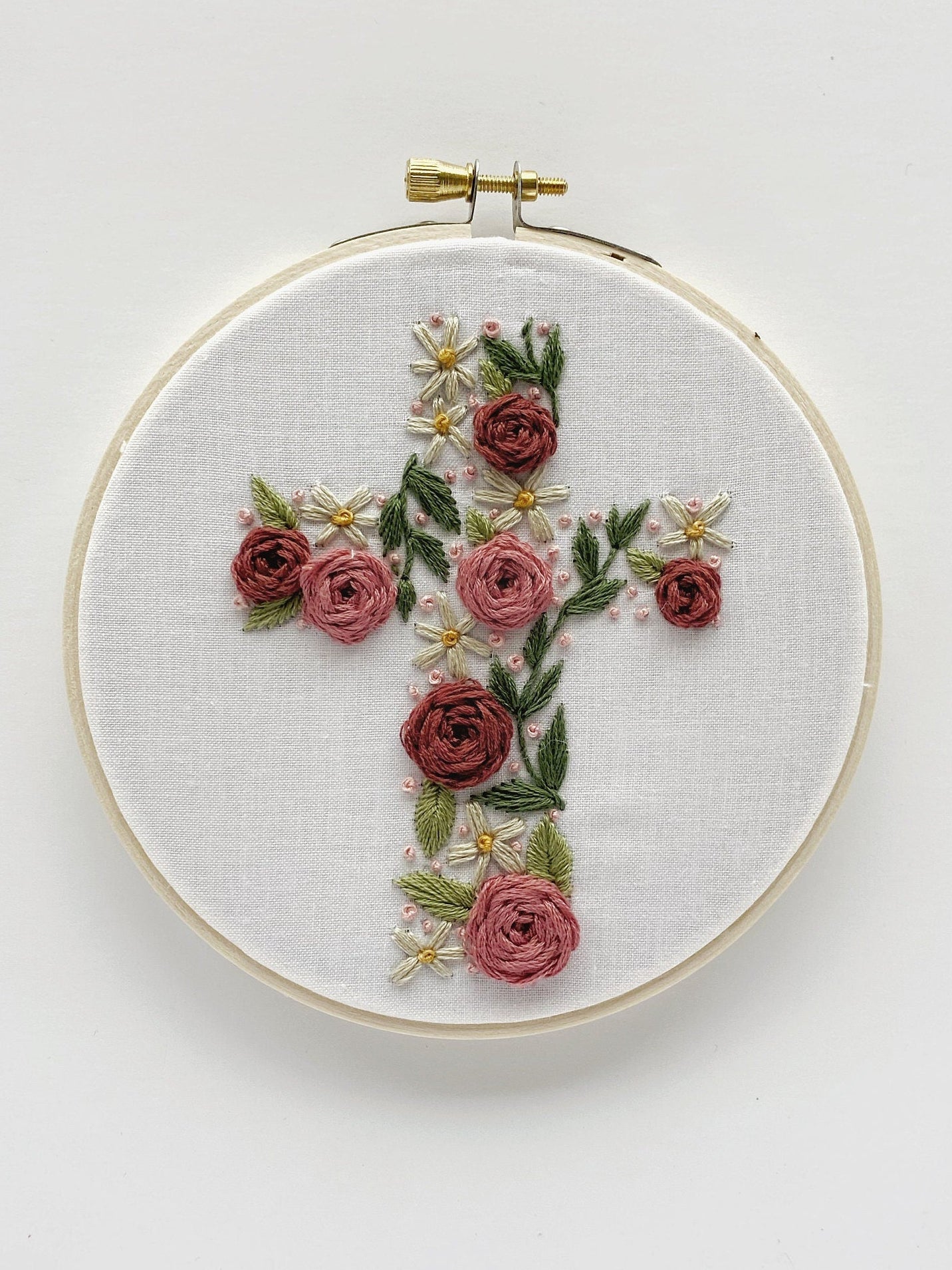 A close up of an floral cross embroidery hoop featuring woven wheel roses for beginner embroidery projects.