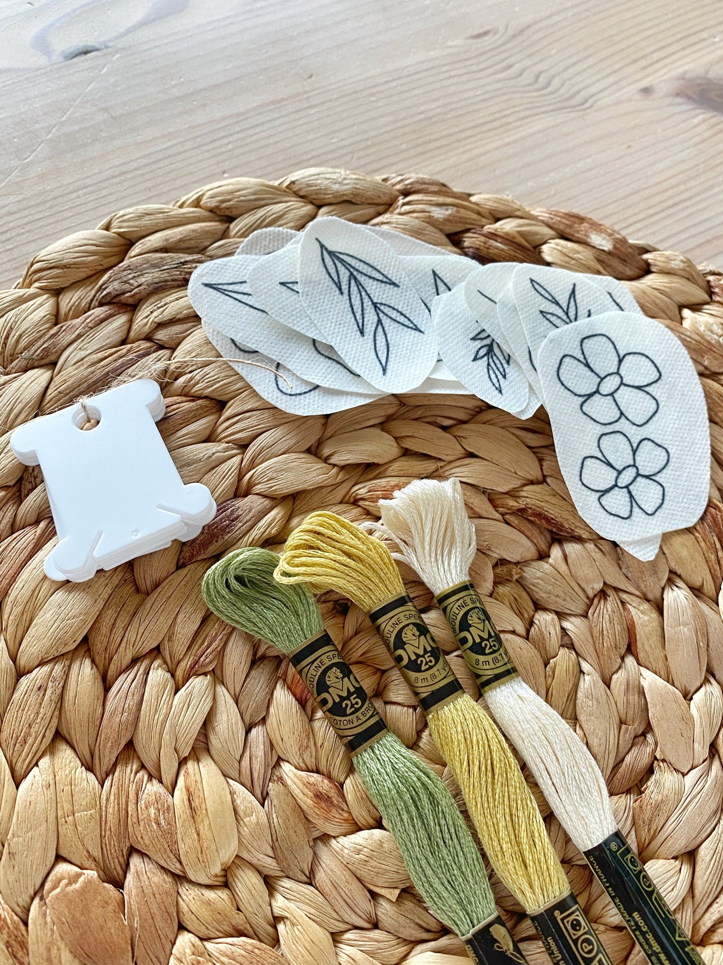 A close up picture of the supplies in a  embroidery kit including floral patterns, threads, and needle.