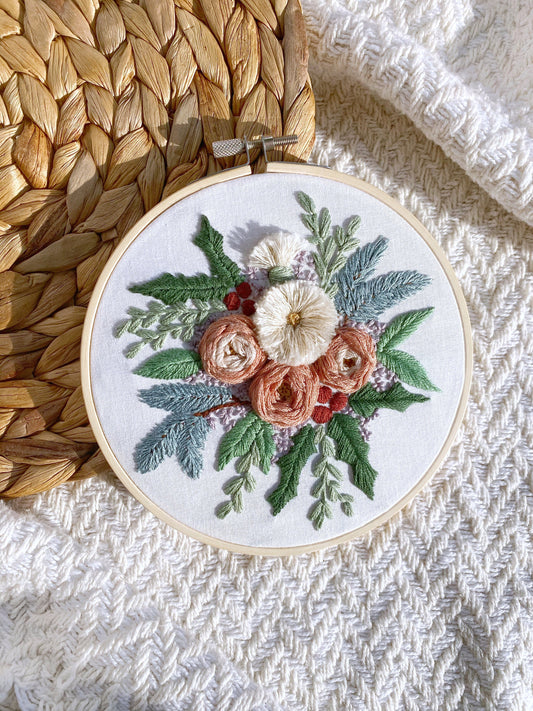Woven wheel embroidered roses and turkey work flowers are surrounded by embroidered wintry foliage and framed in a 6 inch embroidery hoop.