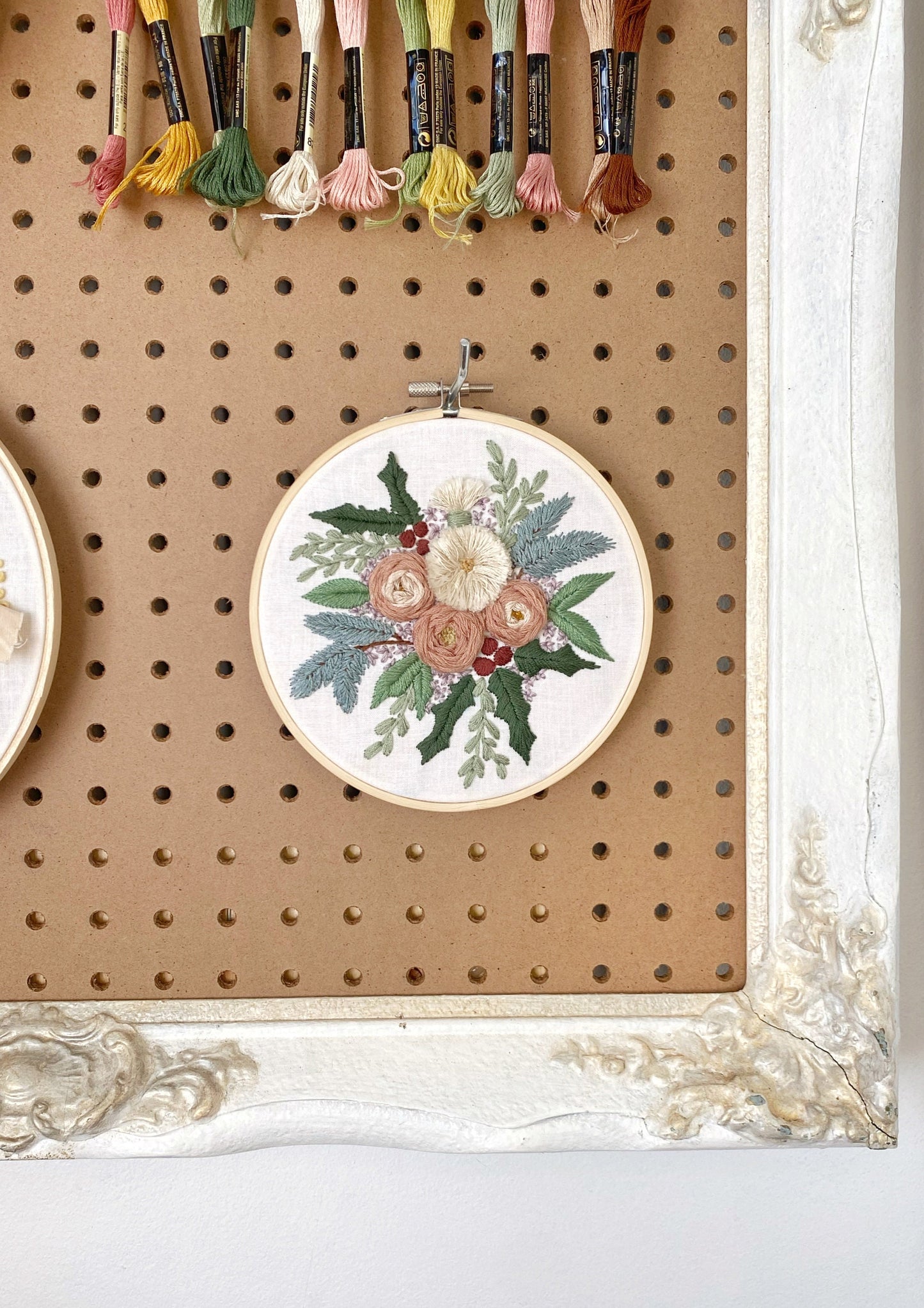 an embroidered floral arrangement featuring an assortment of textured flowers surrounded in wintery foliage including stitched pine boughs and holly displayed for embroidery inspiration.