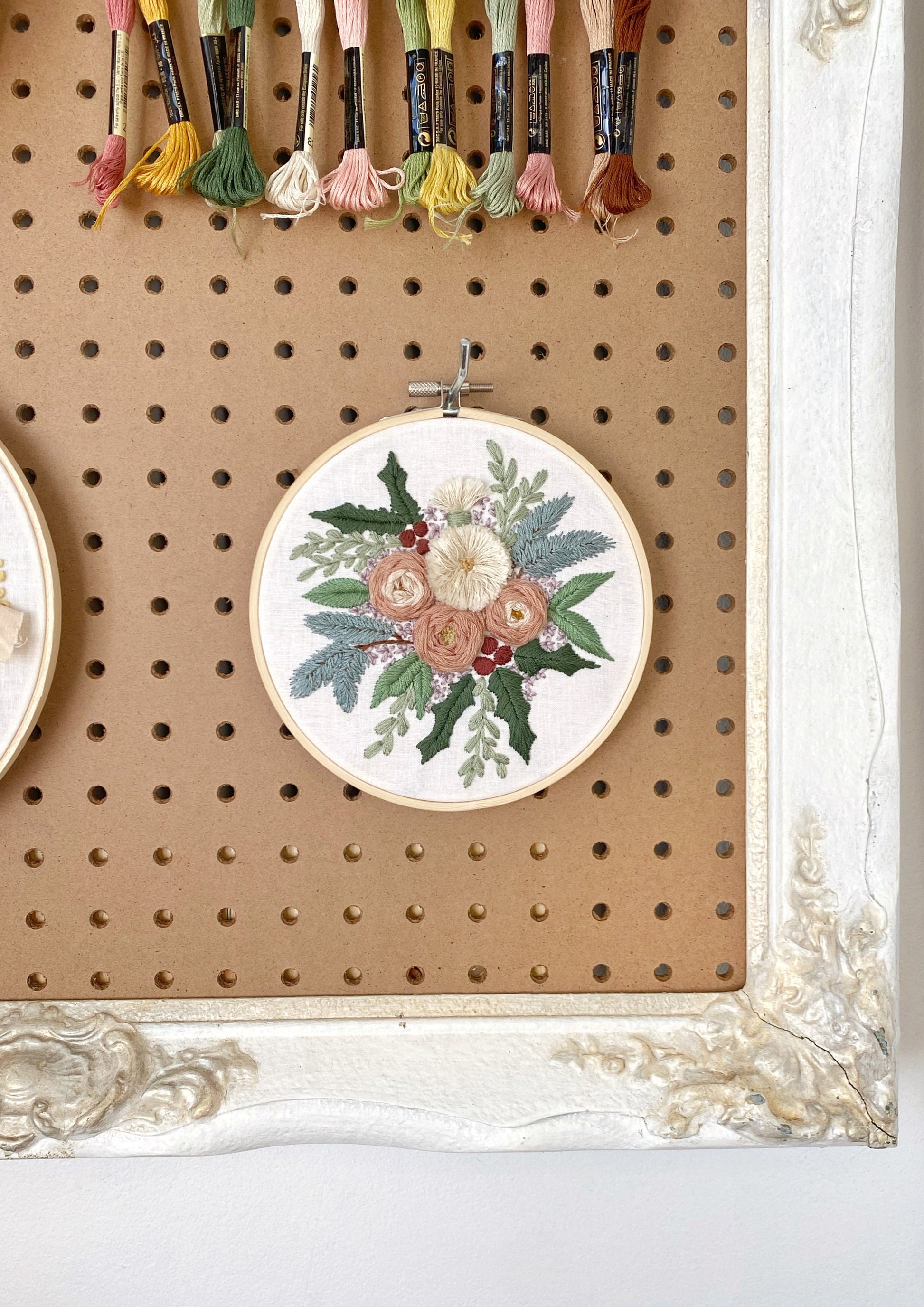 an embroidered floral arrangement featuring an assortment of textured flowers surrounded in wintery foliage including stitched pine boughs and holly displayed for embroidery inspiration.